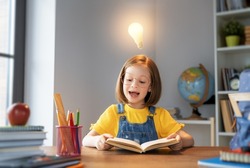 Back to school! Happy cute industrious child is sitting at a desk indoors. Kid is learning in class or lesson. A light bulb overhead as a metaphor for an idea.
