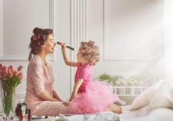 Happy loving family. Mother and daughter are doing hair and having fun. Mother and daughter doing your makeup sitting on the bed in the bedroom.