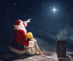 Merry Christmas and happy holidays! Cute little child girl and Santa Claus sitting on the roof and looking at Christmas star. Christmas legend concept.