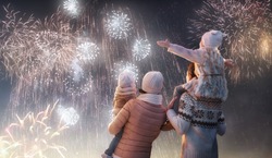 New Year holiday. Happy family, parents and daughters children girls are watching fireworks. The child sits on the shoulders of his father on snowy winter walk in nature. Holidays winter season.