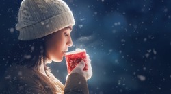 Happy young woman with a cup of hot tea on snowy winter walk in nature. Concept of frost winter season.