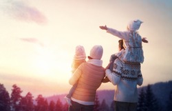 Happy family at sunset. Father, mother and two children daughters are having fun and playing on snowy winter walk in nature. The child sits on the shoulders of his father. Frost winter season.