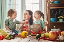 Healthy food at home. Happy family in the kitchen. Mother and children daughters are preparing the vegetables and fruit.