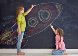 Back to school! Two happy cute industrious children are drawing rocket on blackboard. Kids are learning in class. 