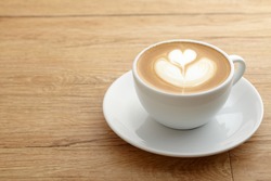 A  cup of coffee with heart pattern in a white cup on wooden background