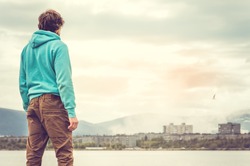 Young Man standing alone outdoor Travel Lifestyle concept with lake and city on background