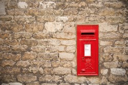 traditional old English red postbox mounted in a cotswold stone wall