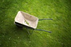 Old rusty wheelbarrow on a green grass field background. Top view perspective used.