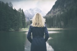 Blonde woman standing backwards and watching magic lake in mountainous country landscape.
