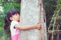 Little Asian girl hugs and kisses a tree.Wild love concept