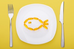 fish oil soft gels lying on white porcelain plate in the form of fish (yellow background)