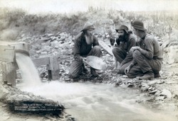 Three men, with dog, panning for gold in a stream in the Black Hills of South Dakota in 1889. Old timers, Spriggs, Lamb and Dillon may be die hard survivors from the Gold Rush of 1876.