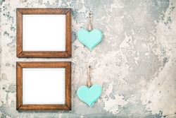 Two photo or picture frames blanks and pair of handmade Valentine's day love hearts hanging on vintage aged grunge textured concrete wall background. Retro old style filtered photo