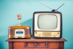 Retro outdated TV set from 60s, old FM radio, golden microphone on oak wooden table front mint blue background. News, press conference or nostalgic music concept. Vintage style filtered photo