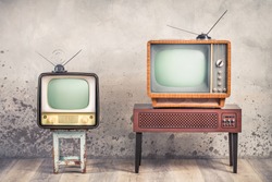 Two old retro classic analog CRT TV set receivers and aged wooden television stand with outdated amplifier front aged concrete wall background. Broadcasting, news concept. Vintage style filtered photo