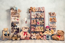 Retro Teddy Bear plush toys great collection on wooden shelving, antique rocking chair, old stool, boxes front loft concrete wall background. Childhood nostalgia concept. Vintage style filtered photo
