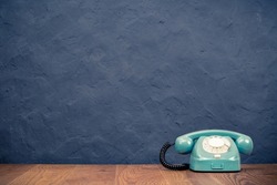 Retro rotary telephone on table front textured black concrete wall background. Vintage old style filtered photo