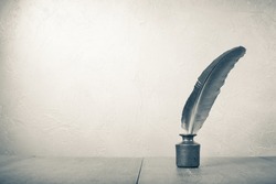 Old quill pen with inkwell on wooden desk. Vintage style sepia photo