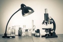 Old laboratory glass, retro microscope and desk lamp. Vintage style sepia photo