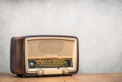 Retro broadcast radio receiver with green eye light on wooden table circa 1950 front concrete wall background. Listen music concept. Vintage instagram old style filtered photo