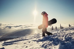 Female snowboarder holding snowboard standing on mountain slop, preparing to snowboarding. Sunny winter day in ski resort