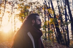 atmospheric autumn outdoor portrait of young man wearing long hair, beard and moustache 