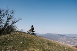 Active elderly man riding enduro motocross motorcycle pit bike in beautiful mountains hills landscape
