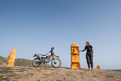 Female traveling on dirt bike motorcycle wearing protection  moto armor jacket standing near the wooden Statues Faces  on sea shore