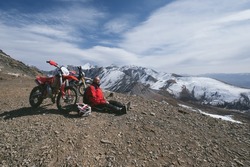 Portrait of 60-year-old Active man with grey hair  resting near enduro motorcycle in beautiful snow mountain landscape
