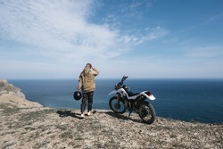 Female rider relaxing in offroad motorcycle travel on mountain top, beautiful sea shore and mountains landscape on background 