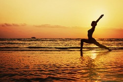Silhouette of young woman doing yoga on the beach in hero pose