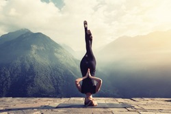 Young woman doing complex Yoga exercise headstand with Namaste asana. Amazing Yoga landscape in beautiful mountains