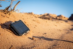 Rugged power bank with solar panel charging electricity in the nature and sand of the desert during a sunny day. Outdoor adventure ensuring charging of your mobile devices. 