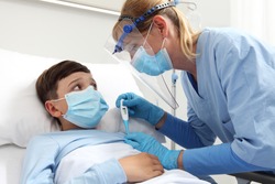 nurse with thermometer measures fever on patient child in hospital bed, wearing protective visor and surgical mask, corona virus covid 19 protection concept, 