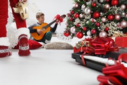 merry christmas and happy holidays, children play guitar and tambourine near the christmas tree with wrapped gift packages and musical instruments, at home in the living room sitting on the floor