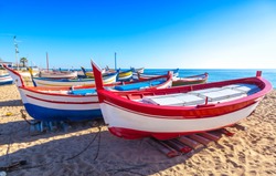 Costa Brava, Spain. Fishing boats rest on a golden sand beach overlooking the blue sea at Calella.
