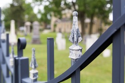 Selective focus on the fence gate of a cemetery.  Grave yard can be seen in soft focus behind it in the background