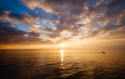Calm sea with sunset sky and sun through the clouds over. Meditation ocean and sky background. Tranquil seascape. Horizon over the water. a little boat sails on a quiet sea