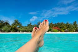 Close-up of female foot in the blue water on the tropical beach. Vacation holidays.