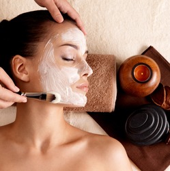 Spa therapy for young woman receiving facial mask at beauty salon - indoors