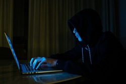 Hacker is  hacking into the computer network. Young boy in a dark room with laptop.  Hacker with a laptop.  Computer criminal. 