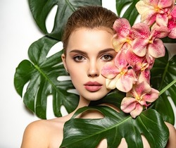Pretty girl in Skin care beauty treatments concept. 
 Beautiful woman with green leave near face and body. Closeup girl's face with green leave. Model with pink tropical orchid near face. 