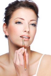Portrait of beautiful woman applying lipstick using lip concealer brush