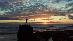 Human with raised hands looks to the sun over horizon in morning while sunrise.  Man stands on a rock against the ocean  beautiful summer sunset. Beauty of nature.  Silhouette of a man against the sky