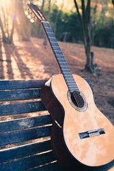 Beautiful classical guitar on a bench in the park with lens flare. Photo of a new wooden guitar with nylon strings outdoors in the summer during sunset. No people. Beautiful string instrument.