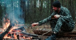 Adult man outdoors is cooking meal on fire. Man roasts sausages on a fire on nature. Person cooks dinner over a fire in the woods. 