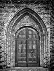 A black and white photo of an arched doorway to a gothic style church.