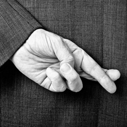 A B/W conceptual image of a business man with his fingers crossed behind his back.