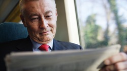 Mature business investor reading a newspaper during a train journey