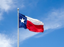 Texas State flag on the pole waving in the wing against blue sky and white clouds